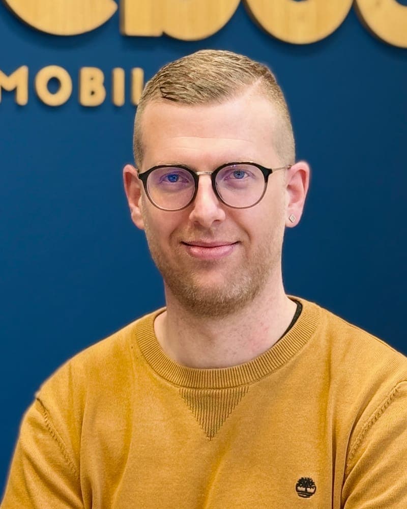 Portrait à lunettes devant le mur bleu de l'agence et son enseigne en bois.