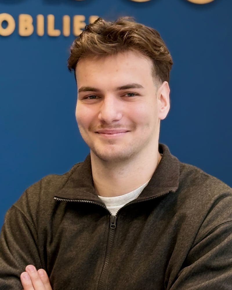 Portrait souriant devant le mur bleu de l'agence et son enseigne en bois.
